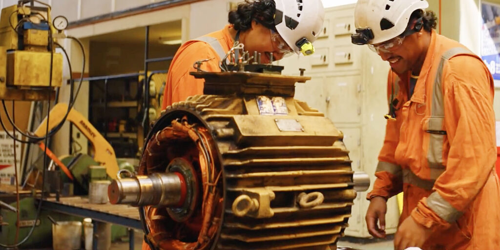Technicians inspecting an industrial motor inside a maintenance facility Technicians inspecting an industrial motor inside a maintenance facility