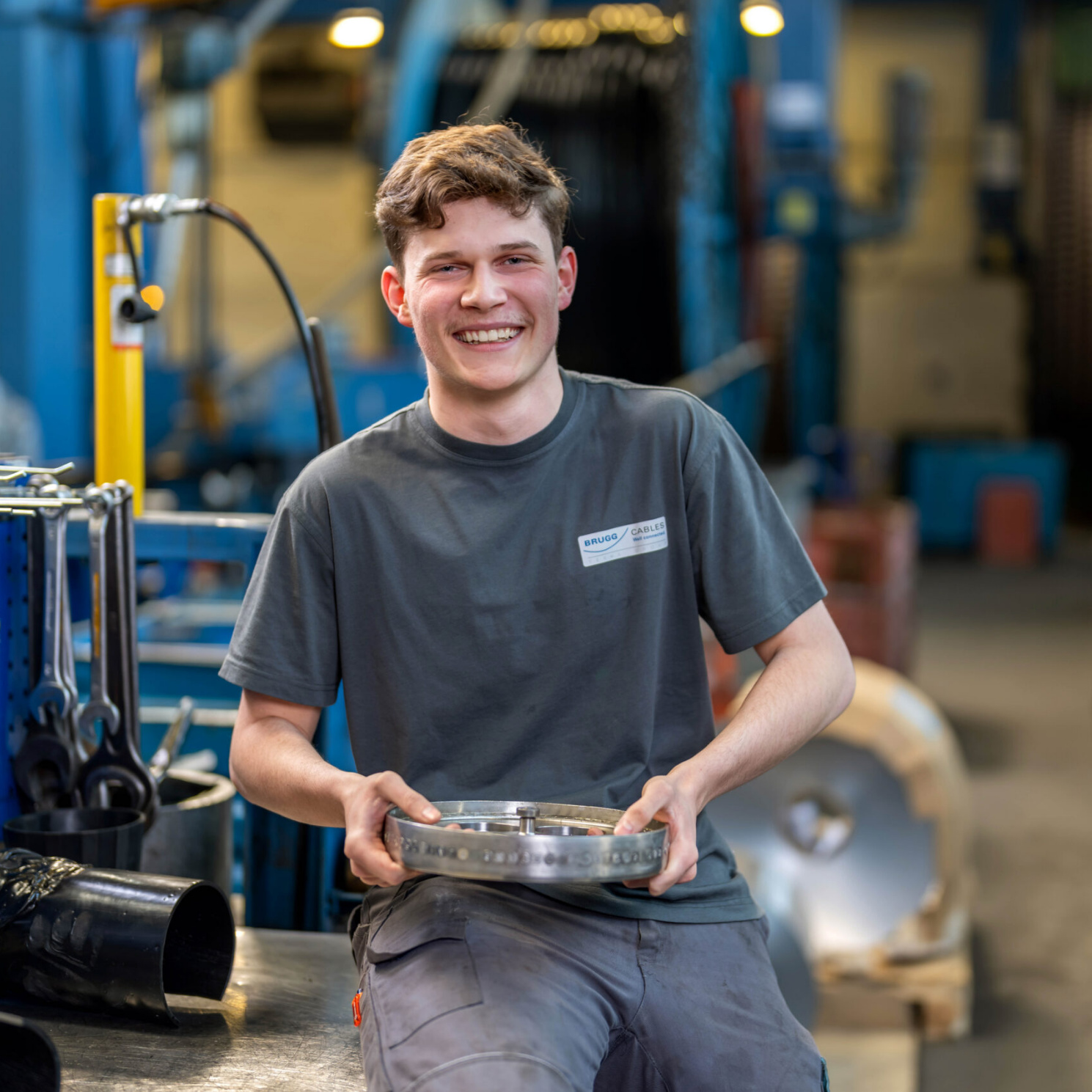 Young apprentice at Brugg Cables holding a cable component in the manufacturing workshop Young apprentice at Brugg Cables holding a cable component in the manufacturing workshop